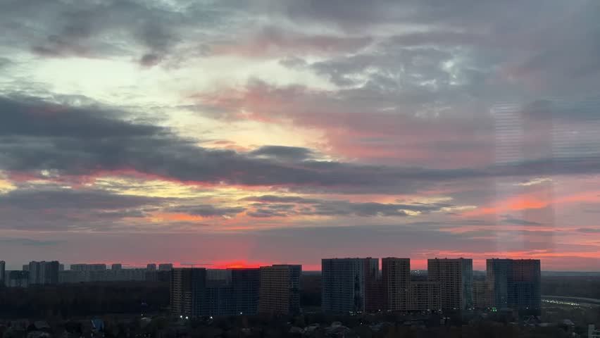 A cityscape at sunset with tall buildings bathed in warm orange and pink light.A short timelapse showing dramatic sky colors and clouds moving over a Moscow city residential skyline at sunset.