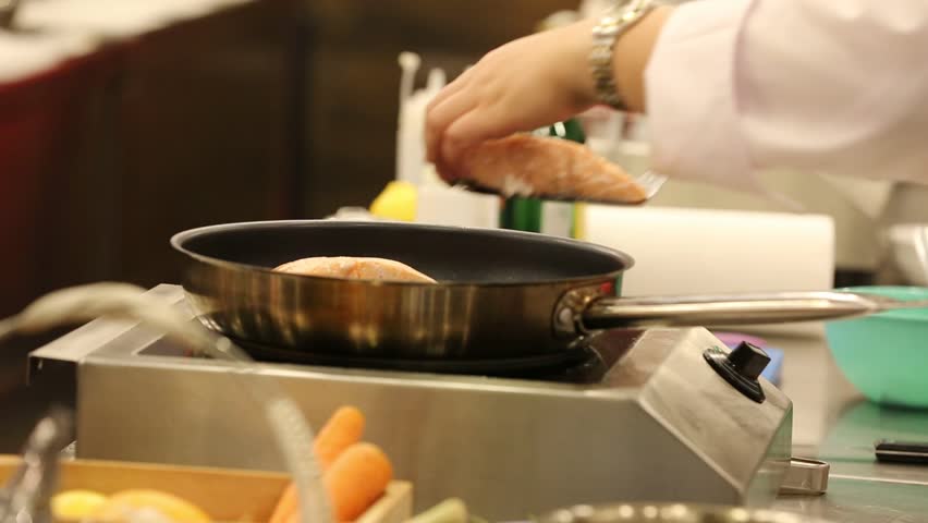 A professional chef is cooking salmon fillet in a pan, it looks appetizing