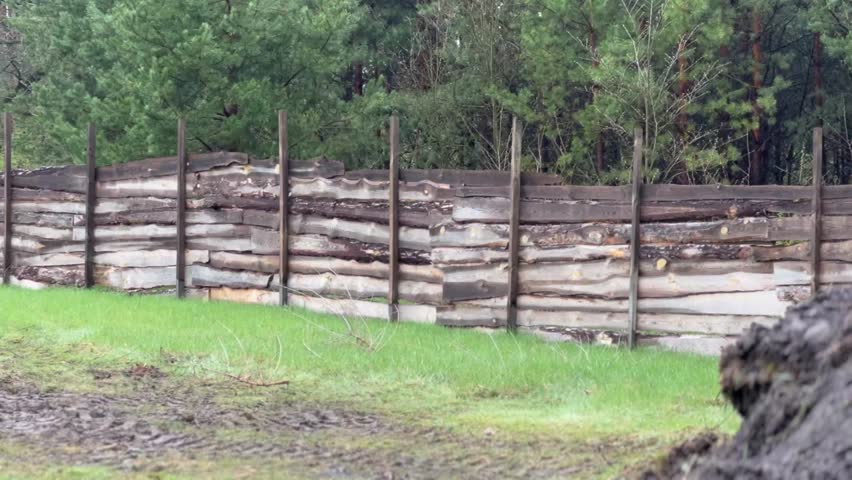 Wooden fencing is being built along a trail in a peaceful forest. The sound of nature complements the sight of trees and greenery as the structure takes shape.