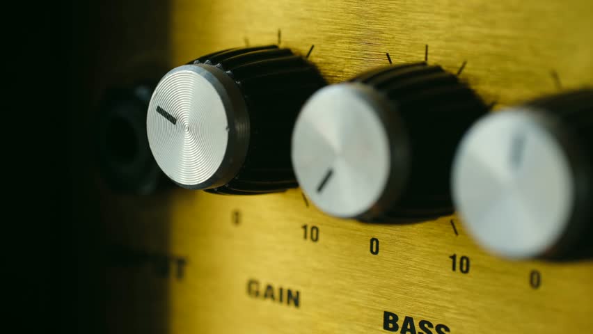 Close up view of a musician hand adjusting the gain and bass knobs on a vintage style yellow guitar amplifier, fine tuning the sound for a perfect musical performance or recording session - Powered by Shutterstock - Get 15% off with code: PIKWIZARD15
