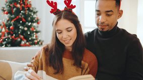 Multiracial couple enjoying a cozy evening by the Christmas tree while reading together this festive New Year - Powered by Shutterstock - Get 15% off with code: PIKWIZARD15
