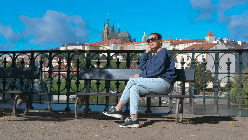 Tourist relaxing on bench enjoying prague castle view. Woman sitting on bench, gazing at historic prague castle during golden afternoon light, overlooking scenic cityscape with river