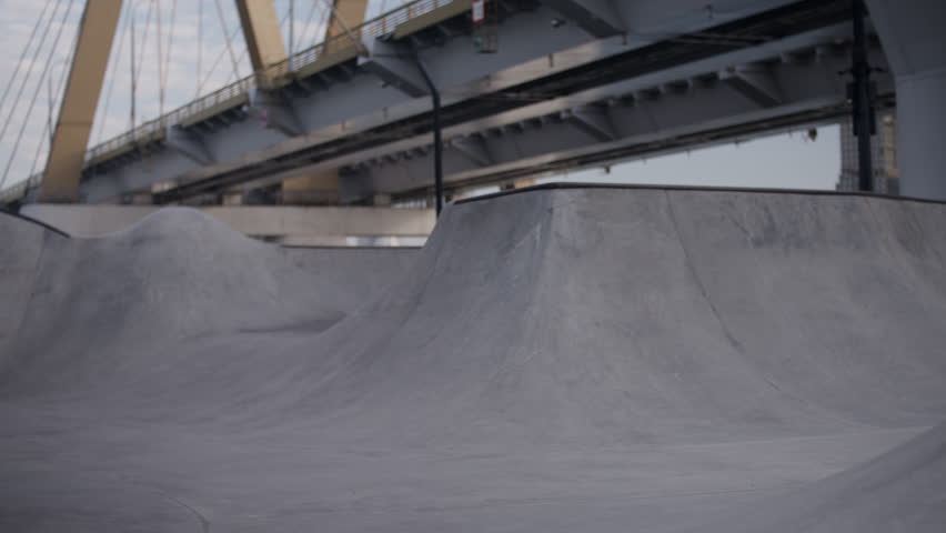Aggressive inline skater rides ramp fast in skate park by bridge