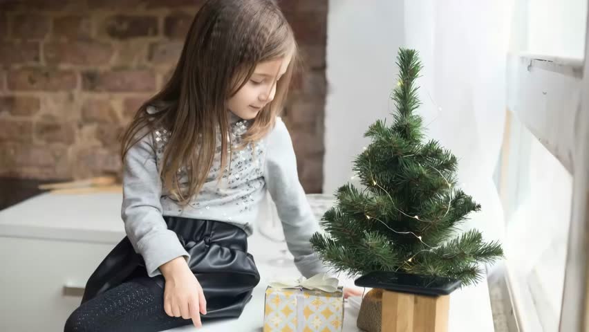 Cute girl decorating a small Christmas tree with lights and gifts.