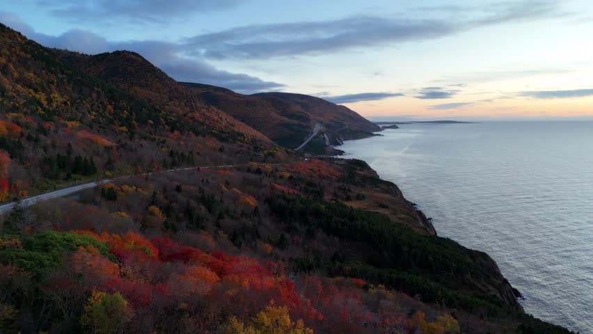 Aerial view of the Cap Rouge Mountains along the Cabot Trail during an onset of a sunset with dramatic clouds overlooking the Atlantic Ocean and the highway	