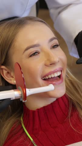 Woman smiling during dental resin curing, brightly lit scene of woman receiving dental bonding