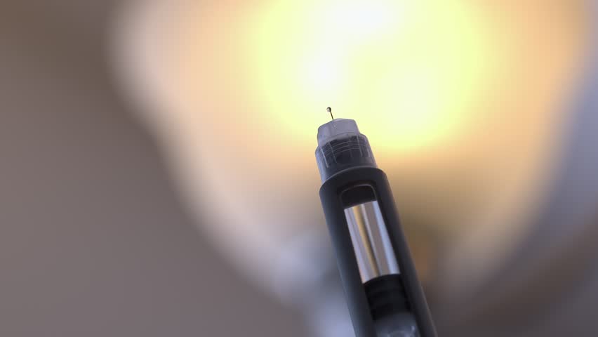 Small drops of medical drug drip out of needle tip of injection pen