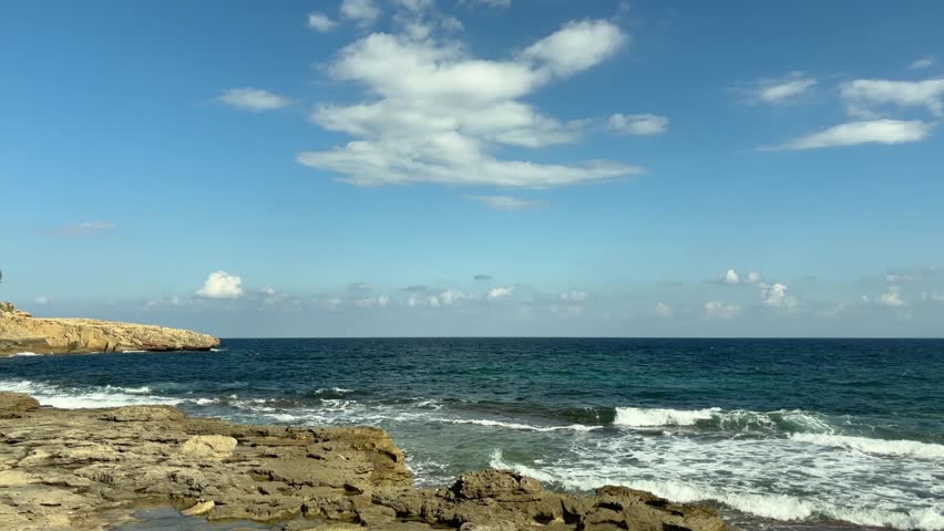 waves crash gently on the rocky shore of cala murada under a bright blue sky in mallorca spain