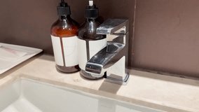 Hand operates chrome faucet, water flows into sink, bright lighting, stationary camera, hotel bathroom - Powered by Shutterstock - Get 15% off with code: PIKWIZARD15