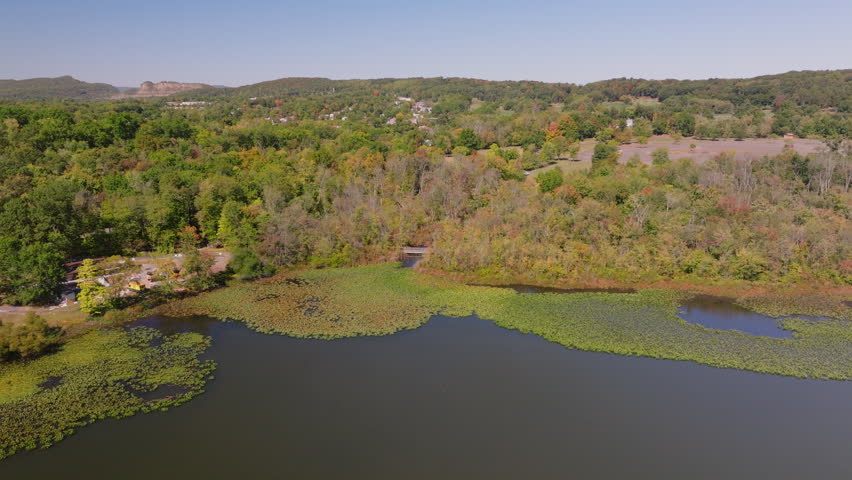 Aerial view of Rockland Lake surrounded by green and autumn trees with patches of water lilies near the shoreline, Rockland County, New York. ProRes HQ422.