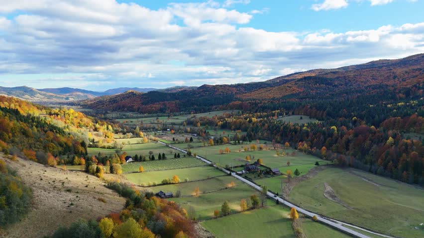 Drone footage showing a car driving through an autumn valley surrounded by colorful forests in Bucovina, Romania