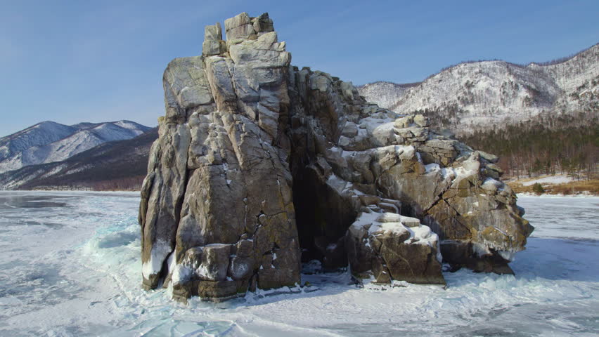 A flight over frozen Lake Baikal. Transparent ice. Sandy bay, Cormorant Rock. Winter journey.