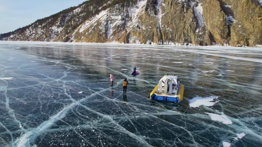 Tourists admire the cracks and transparency of the ice of Lake Baikal. Winter trip on a hovercraft on a frozen lake. 