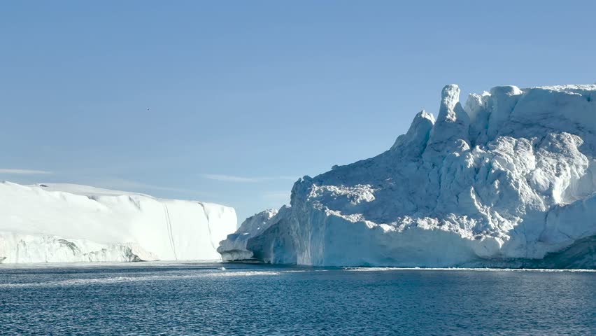 Giant iceberg drifts in calm waters under clear blue sky in the Arctic region