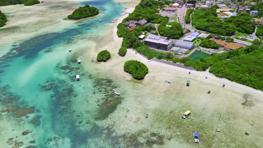 Aerial drone footage pans over the stunning turquoise waters and green islets of Kabira Bay, Ishigaki, Okinawa, Japan. A beautiful, sunny day in a tropical paradise with tour boats below.