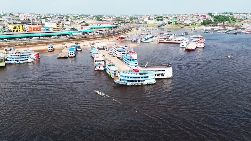 Aerial view of passenger boats docked at the main river terminal in Manaus, Brazil, where vessels, small boats, and people navigate the busy Amazon waterfront under bright daylight