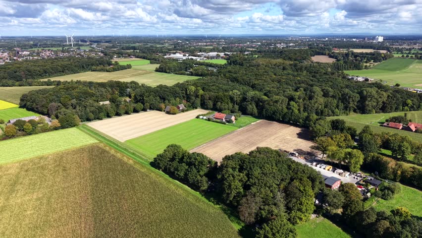 Peaceful landscape with colored green trees and farmland fields in US. Cloudy and sunny day in Fall. Rural area with cultivated corn and cropland. Aerial wide shot. Wind turbine and farmstead.