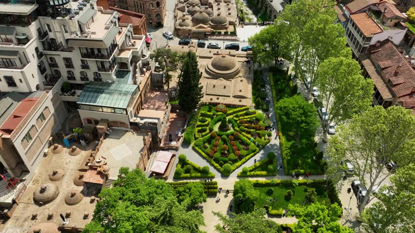 Drone view the greenery of Tbilisi Botanical Garden area and the nearby Abanotubani sulfur baths, surrounded by traditional buildings and tree-filled courtyards