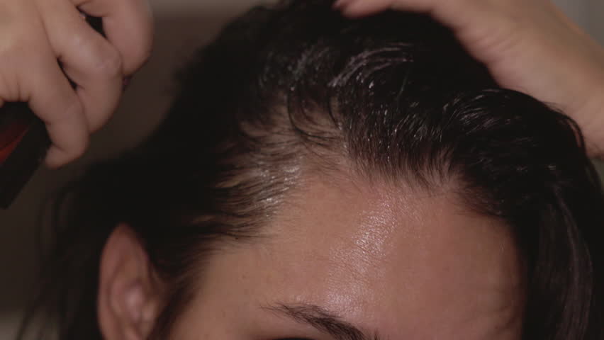 Woman in bathroom applying hair oil and spray for growth and strength. Half of her face visible, focusing on hair care routine. Castor and rosemary oil treatment for healthy shiny roots and hair loss 