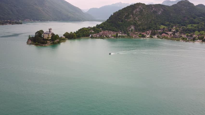 A speed boat towing a wake boarder next to Château de Duingt on Lake Annecy. Amazing scene with the boat shooting across the lake with amazing views in the background. Boat is heading towards.