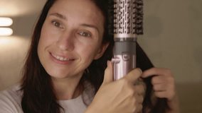 Millennial woman drying and styling her brunette hair with a hair dryer and a rotating brush. She smiles, sings, and dances in a bright minimalist bedroom. Concept of beauty, hairstyle, and self care. - Powered by Shutterstock - Get 15% off with code: PIKWIZARD15