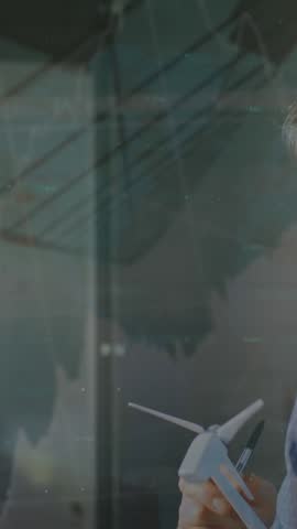 Animation of graphs, numbers over caucasian engineer inspecting windmill model and writing in book. Digital composite, multiple exposure, report, finance, growth, sustainable energy and technology.