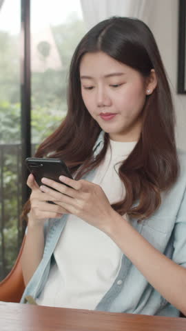 Vertical Screen : Freelance Asian women using mobile phone at cafe. Young Japanese Asian girl using smartphone checking social media on the internet on the table at coffee shop concept.