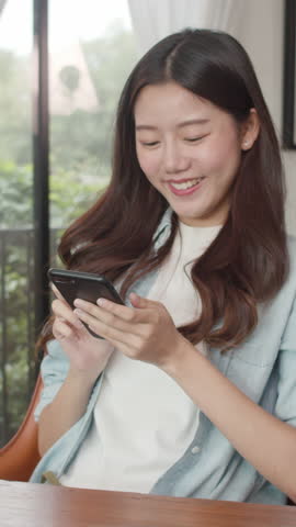 Vertical Screen : Freelance Asian women using mobile phone at cafe. Young Japanese Asian girl using smartphone checking social media on the internet on the table at coffee shop concept.