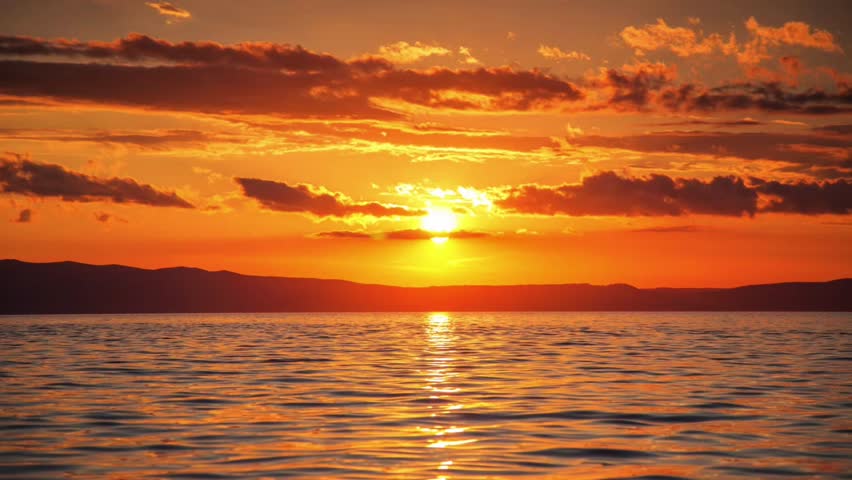 Breathtaking Golden Orange Sunset or Sunrise Over Water and Mountain Silhouettes