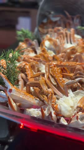 Vertical video of blue crabs with orange shells arranged on ice tray with herbs in seafood display