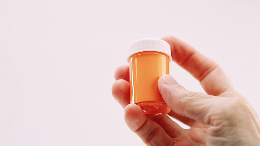 Close-up framing of hand holding and turning an orange acrylic tempera container