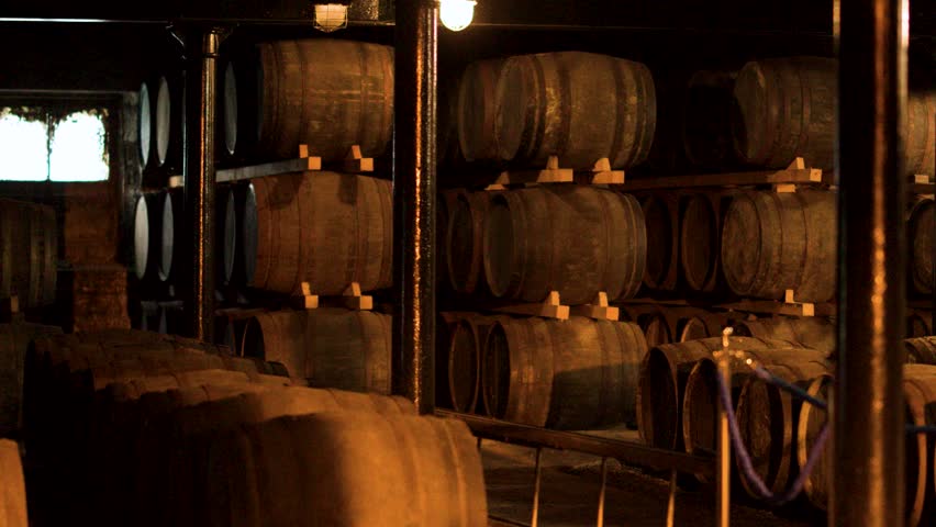 Rows of oak barrels aging whisky in dimly lit Highland warehouse, slow lateral camera movement