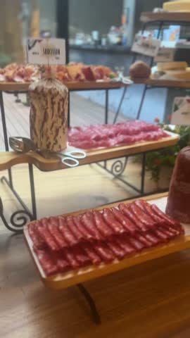 Vertical video of sliced cured meats on wooden trays with sausage and salami in buffet display