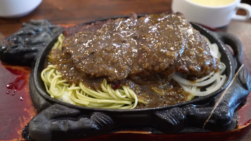Taiwanese style special hot sizzling beef steak with noodles, egg and sauce on an hot iron board plate.