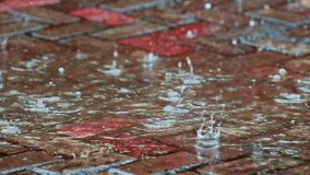 Slow motion video of raindrops hitting the conblock surface, showing water splashes and ripples during a rainy day with reflective wet pavement. - Powered by Shutterstock - Get 15% off with code: PIKWIZARD15