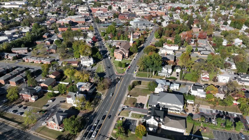 Street junction of American town during sunny day and green trees. Aerial wide shot. Housing area of Harrisonburg and downtown in background. Virginia, USA. Quiet and peaceful neighborhoods. Road fork