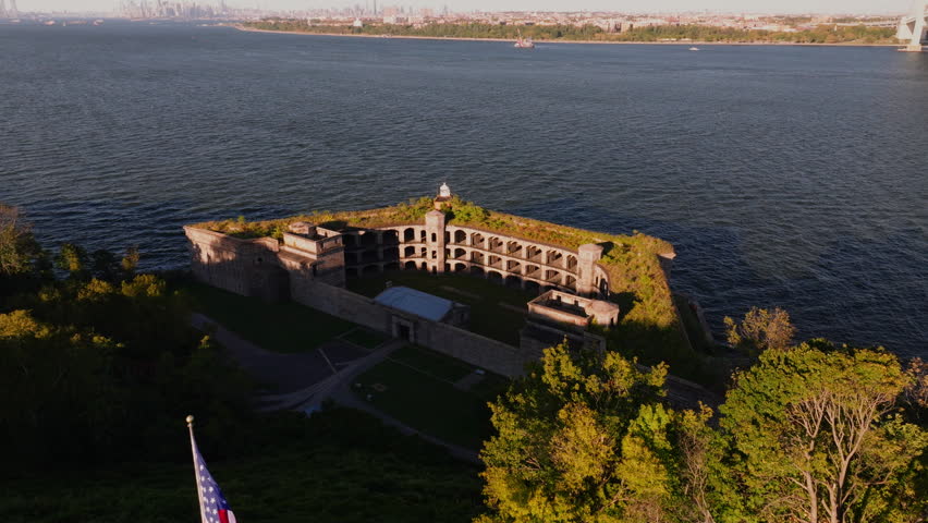 Close-up aerial view of Battery Weed historic fort in Staten Island, New York, showing detailed stone walls, arched passages, and greenery on top under clear blue sky. ProRes HQ422.