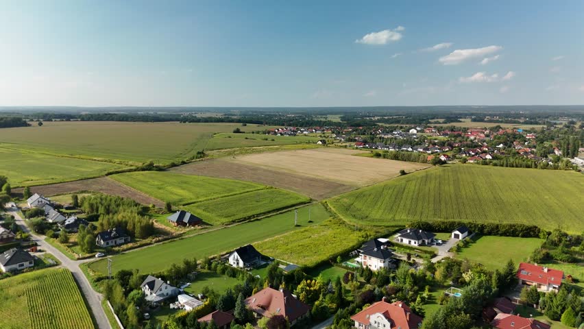 Charming Village in Mountain Region with Country Road, Green Fields, and Blue Sky