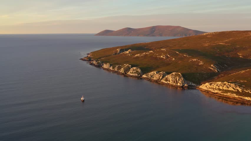 drone arc shot of a small ship near shore in calm sea conditions in the falkland islands at sunset
