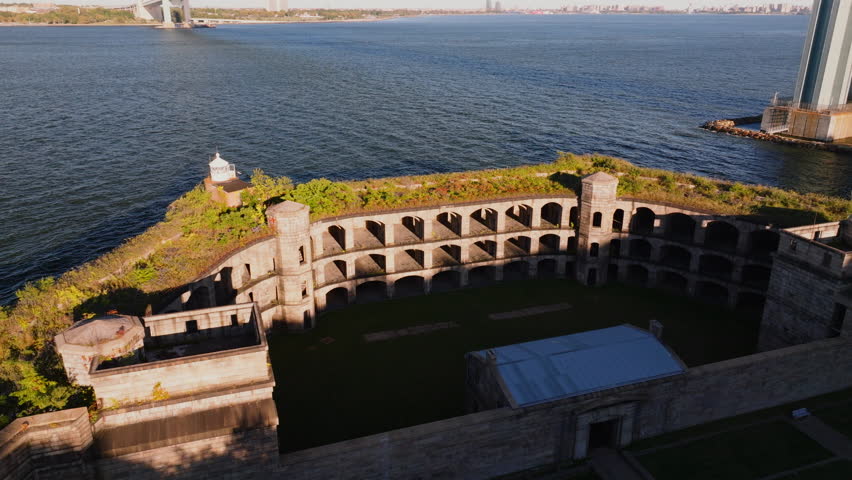 Close-up aerial view of Battery Weed historic fort in Staten Island, New York, showing detailed stone walls, arched passages, and greenery on top under clear blue sky. ProRes HQ422.