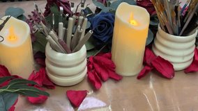 A festive, cozy close-up video clip of a creative work surface decorated with holiday or seasonal crafting supplies. The focus is on two flickering LED pillar candles and two decorative ceramic pots - Powered by Shutterstock - Get 15% off with code: PIKWIZARD15