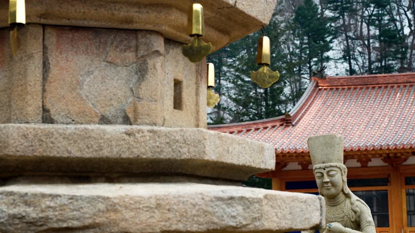 Close-up of an ancient stone pagoda with golden wind chimes and a Buddhist statue at Sangwonsa Temple in Pyeongchang South Korea