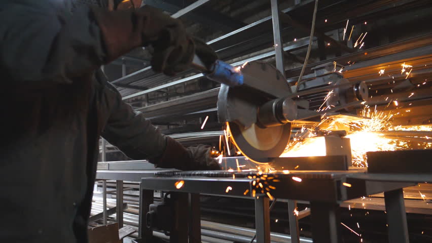 Craftsman with circular saw sawing steel in workshop. Man use saw cutting machine to cut metal. Industrial professional worker in safety protection wear grinding metal. Sparks fly from hot metal