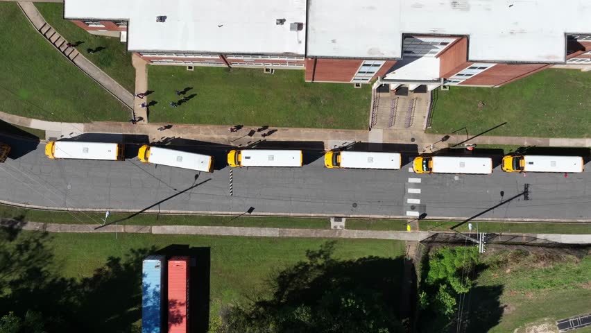 Aerial top down shot showing row of traditional american school buses in row. Sunny in american school area. Summer season with cars on parking area