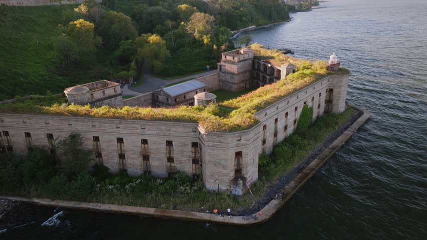 Close-up aerial view of Battery Weed historic fort in Staten Island, New York, showing detailed stone walls, arched passages, and greenery on top under clear blue sky. ProRes HQ422.