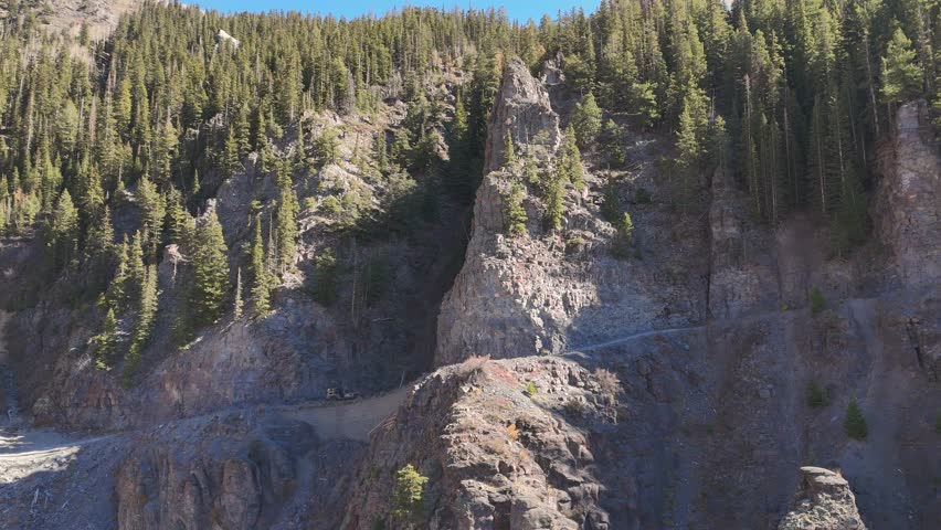 Aerial view of rugged mountainsides with a path winding through the dense trees, showcasing the natural beauty, Telluride, Colorado, United States.