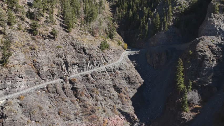 Aerial view of a winding road carved into the side of a steep mountain with evergreens, contrasting shadows and light, Telluride, Colorado, United States.