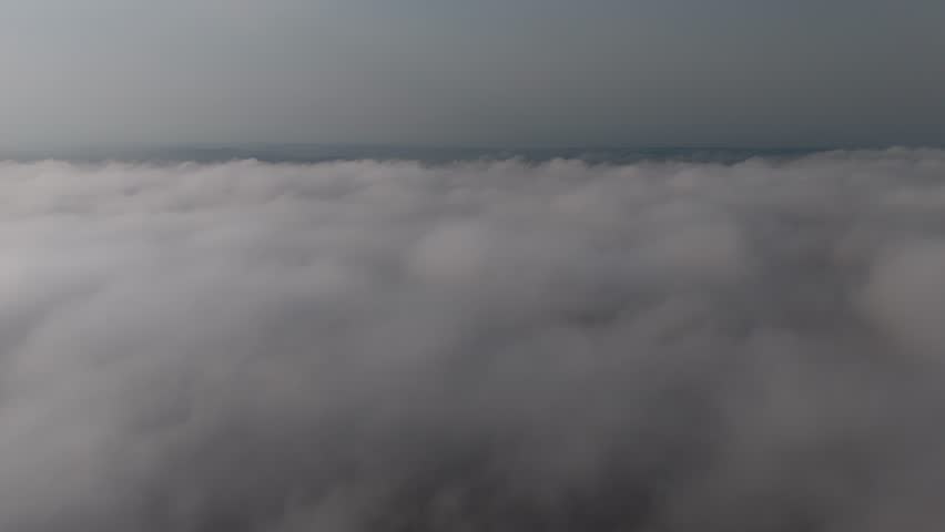 Slow motion aerial shot showing a sea of clouds at sunrise, with low sunlight highlighting the cloud tops.