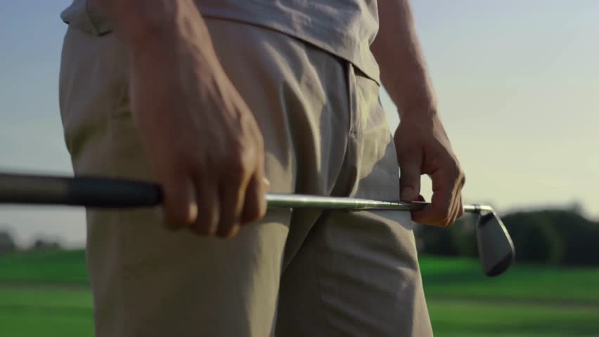 Golfer grips club with focus and determination on tranquil green course while vibrant sunset casts warm glow over the landscape.