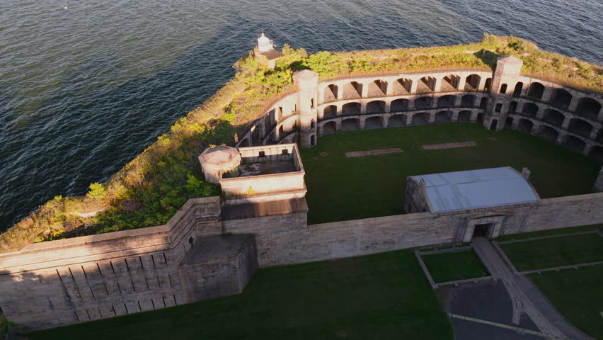 Close-up aerial view of Battery Weed historic fort in Staten Island, New York, showing detailed stone walls, arched passages, and greenery on top under clear blue sky. ProRes HQ422.